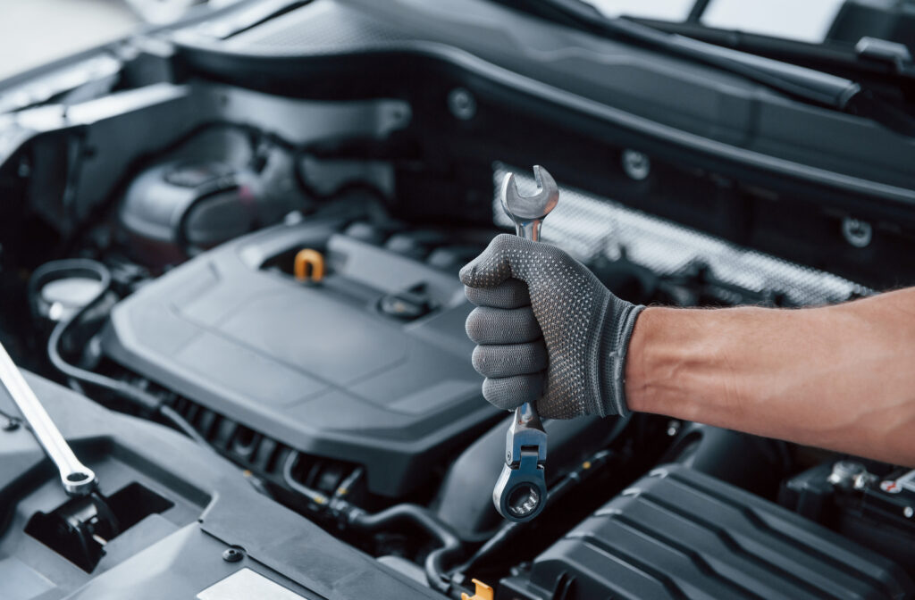 Everything will be fixed. Man's hand in glove holds wrench in front of broken automobile.